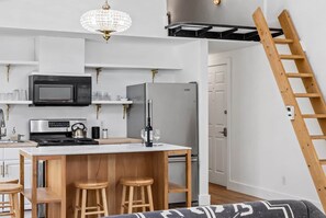 A compact kitchen with a microwave, stove, and refrigerator, a wooden bar stool area, and a chandelier. - Studio 106: Hot Tub, Patio & Parking (Telluride)
