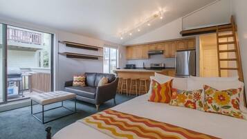 A compact hotel room with a bed, a sofa, a small dining area, and a kitchenette.