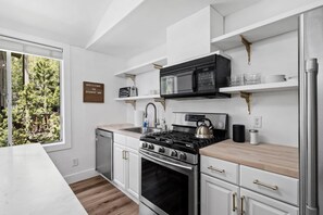 Une cuisine moderne équipée d’une cuisinière à gaz, d’un four et d’un four à micro-ondes. Les meubles sont blancs et le plan de travail est en bois. Une pancarte sur le mur porte l’inscription : « BIENVENUE AU STUDIO 106 ».