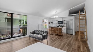 Een modern appartement met een grote schuifpui, een keuken met een centraal eiland en een slaapkamer in loftstijl met een houten trap.