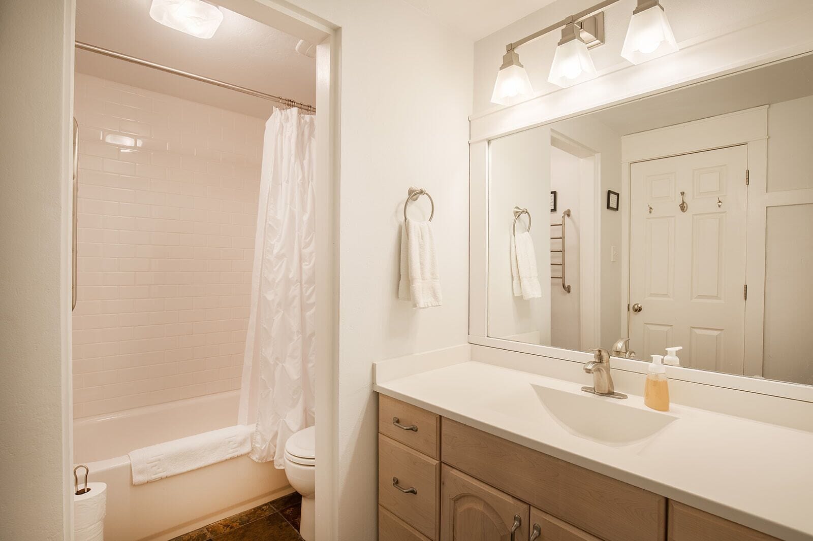 A bathroom with a shower, toilet, sink, and a large mirror.