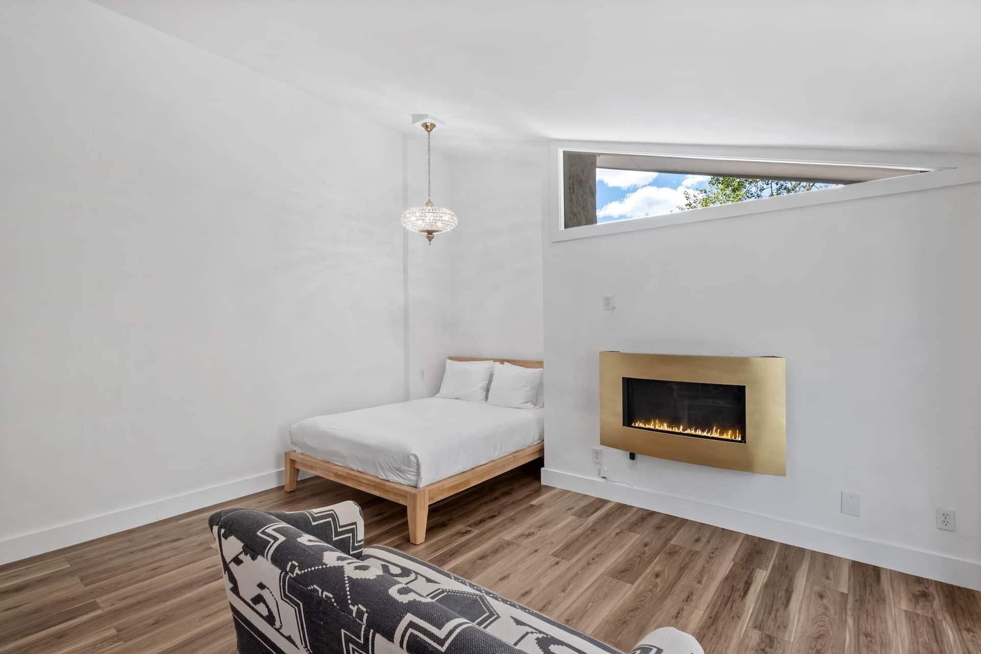 Une chambre à coucher avec un lit, un luminaire suspendu, une cheminée et une fenêtre.