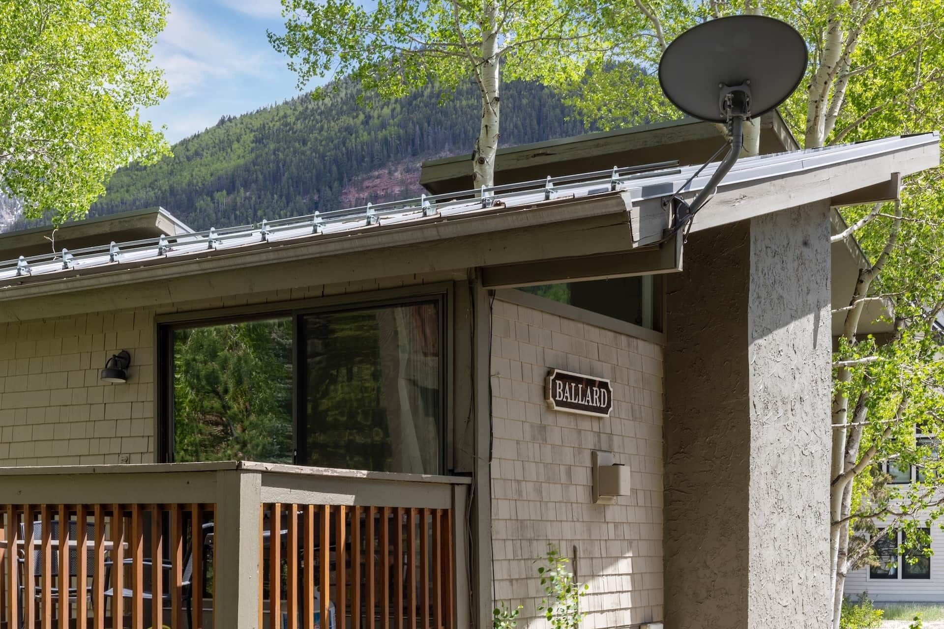 A building with a satellite dish, a sign reading 'BALLARD,' and a view of a forested mountain.