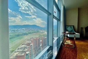 A room with a large window offering a cityscape view, a round table, and a chair. - Hongbo Hotel (Gengma)