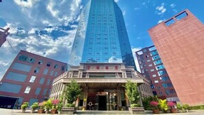 A modern hotel with a prominent glass facade, a traditional entrance, and a red building to the right. - Hongbo Hotel (Gengma)