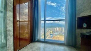 A room with a large window offering a city view, a wooden door, and a marble floor. - Hongbo Hotel (Gengma)
