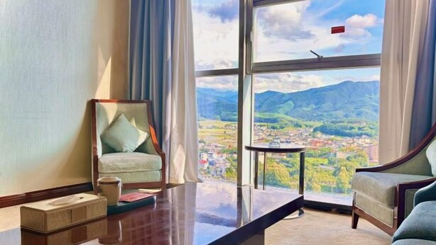 Habitación de hotel con un ventanal grande, un escritorio de madera, una silla y un sofá.