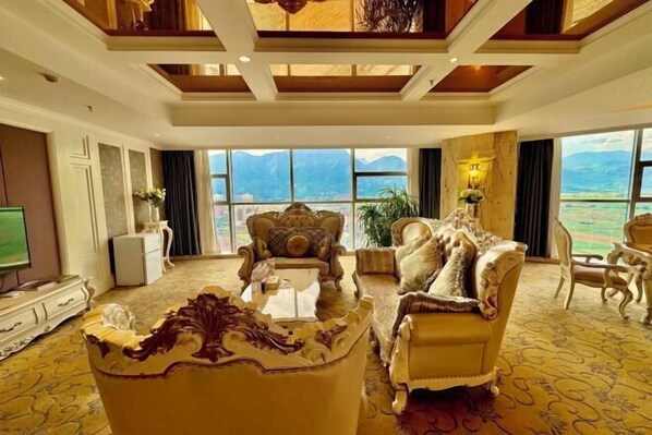 A luxurious living room with ornate furniture, a large window offering a mountain view, and a high ceiling with wooden beams.