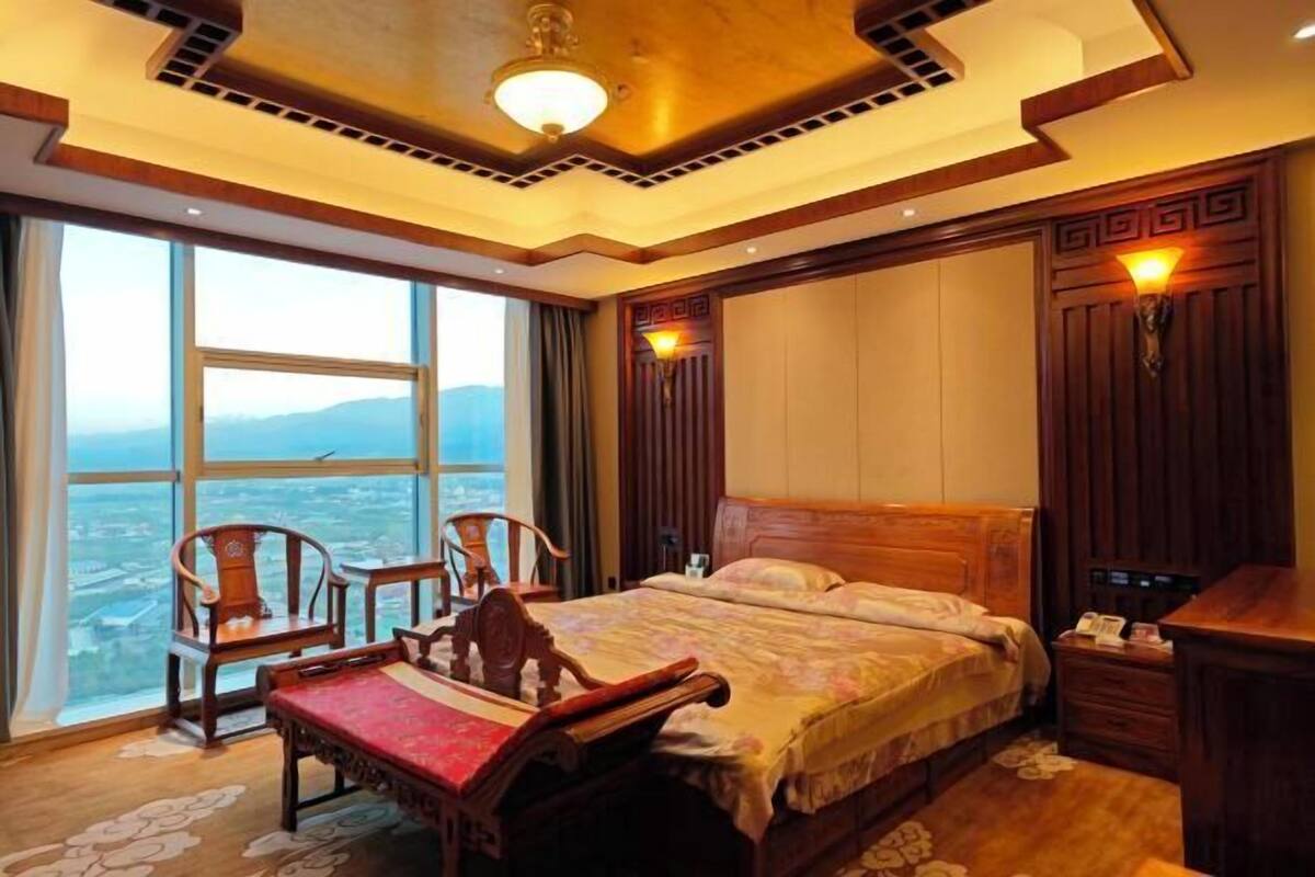 A hotel room with a large window, a bed, a desk, and a chair.