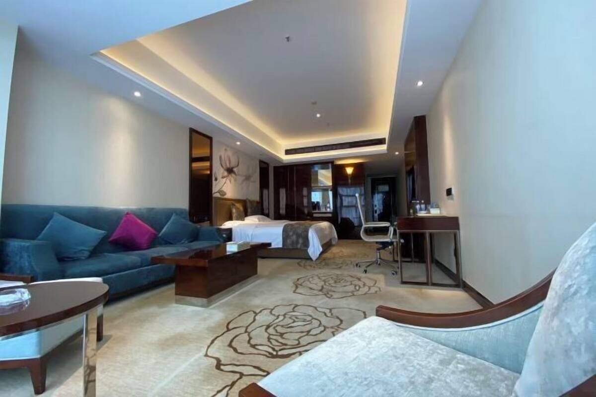 A modern hotel room with a large bed, a sofa, a desk, and a chair.