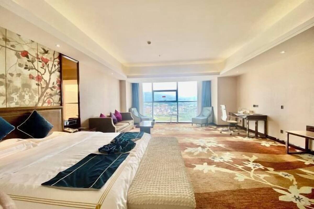 A hotel room with a large bed, a desk, a chair, and a view of the outdoors.
