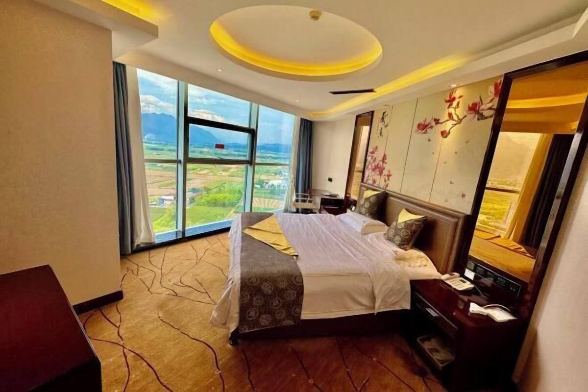 A hotel room with a large bed, a desk, and a view of the countryside.