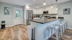 A modern kitchen with white cabinets, stainless steel appliances, and a central island with bar stools. - Seascape - Blue🐬 PRIVATE POOL✔️3-MIN WALK to BCH✔️ (Butler Beach)