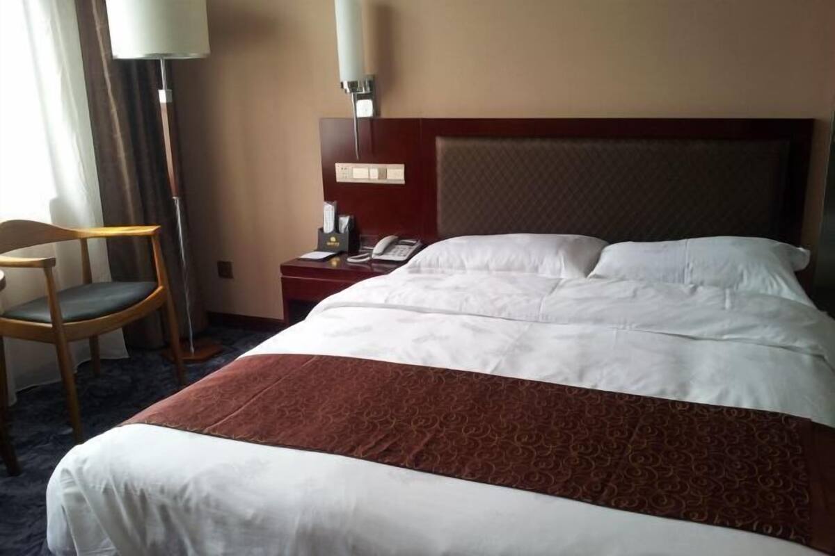 A hotel room with a bed, a chair, a nightstand with a lamp, and a telephone.