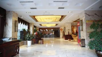 Un vestíbulo de hotel con piso de mármol, una recepción y una araña de cristal.