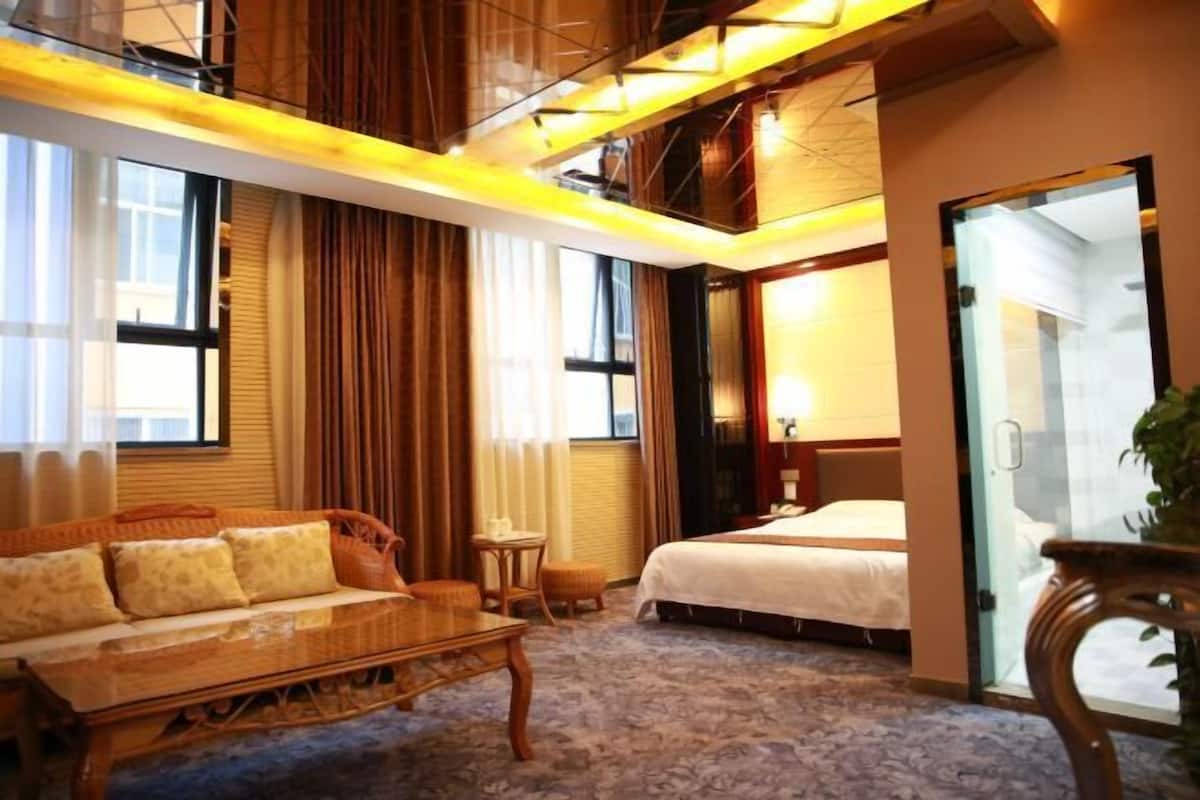 A hotel room with a sofa, a small table, a bed, and a glass door leading to a balcony.