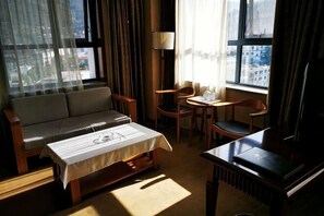 A hotel room with a sofa, a small table, a chair, a lamp, and a piano. - Zhenghe Holiday Hotel (Zhen'an)