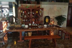 A dining area with a long wooden table, benches, and a decorative shelf with various items. - Zhenghe Holiday Hotel (Zhen'an)