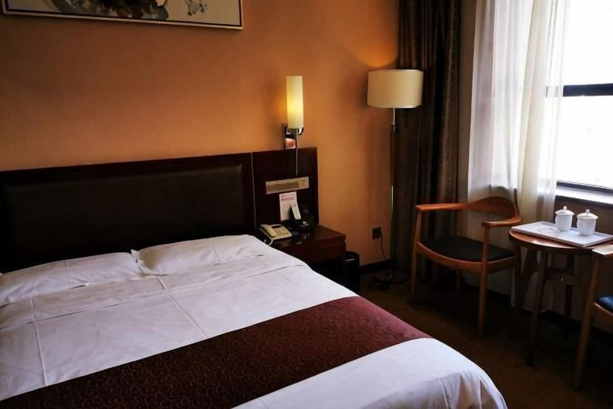 A hotel room with a large bed, a bedside table with a lamp, a chair, and a small table with a lamp.