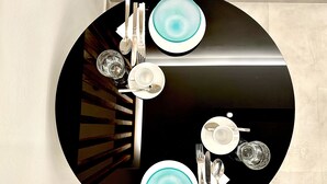 Un tavolo da pranzo rotondo con piano nero, piatti bianchi decorati con motivi blu, posate e bicchieri trasparenti.