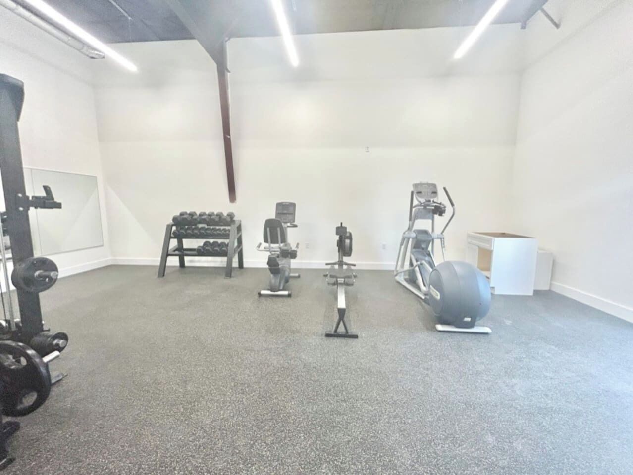 A gym with various exercise equipment including dumbbells, a bench press, a stationary bike, and a rowing machine.
