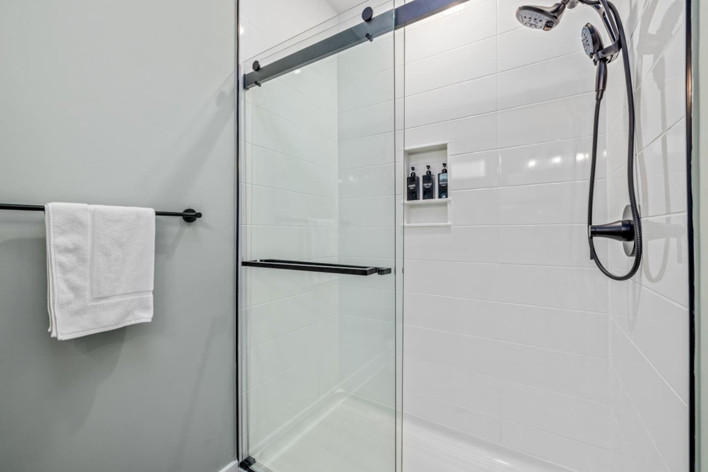 A modern shower with a glass door, a towel rack, and a shelf with toiletries.