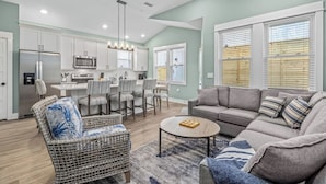 A modern kitchen with white cabinets, stainless steel appliances, and a dining area with striped chairs. - Brand New Single Level Condo, Steps from the Beach  (Corolla)