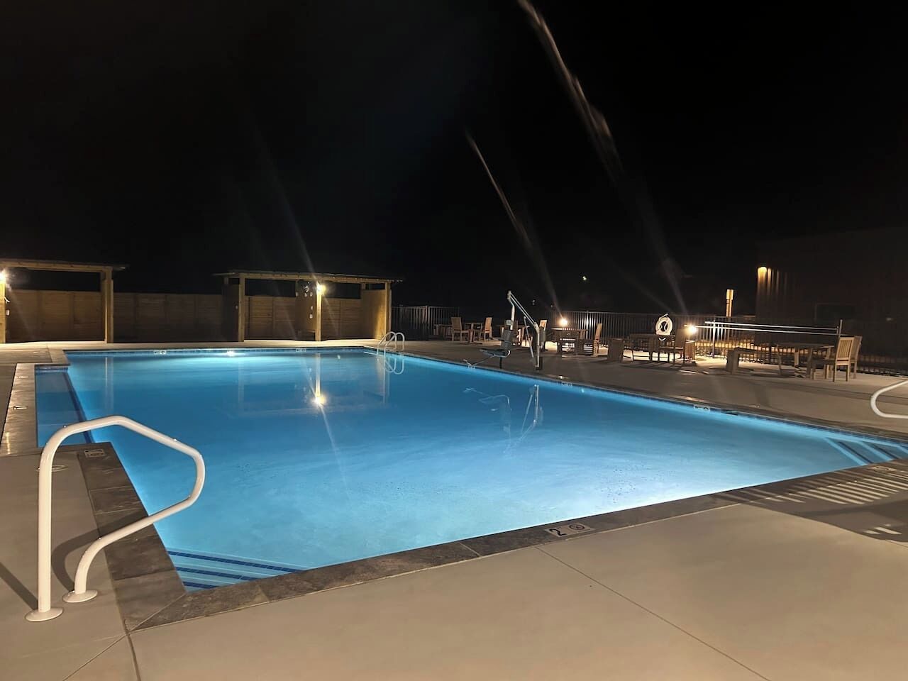 Une piscine nocturne à l’eau claire, entourée de chaises longues et d’un espace de repos abrité.