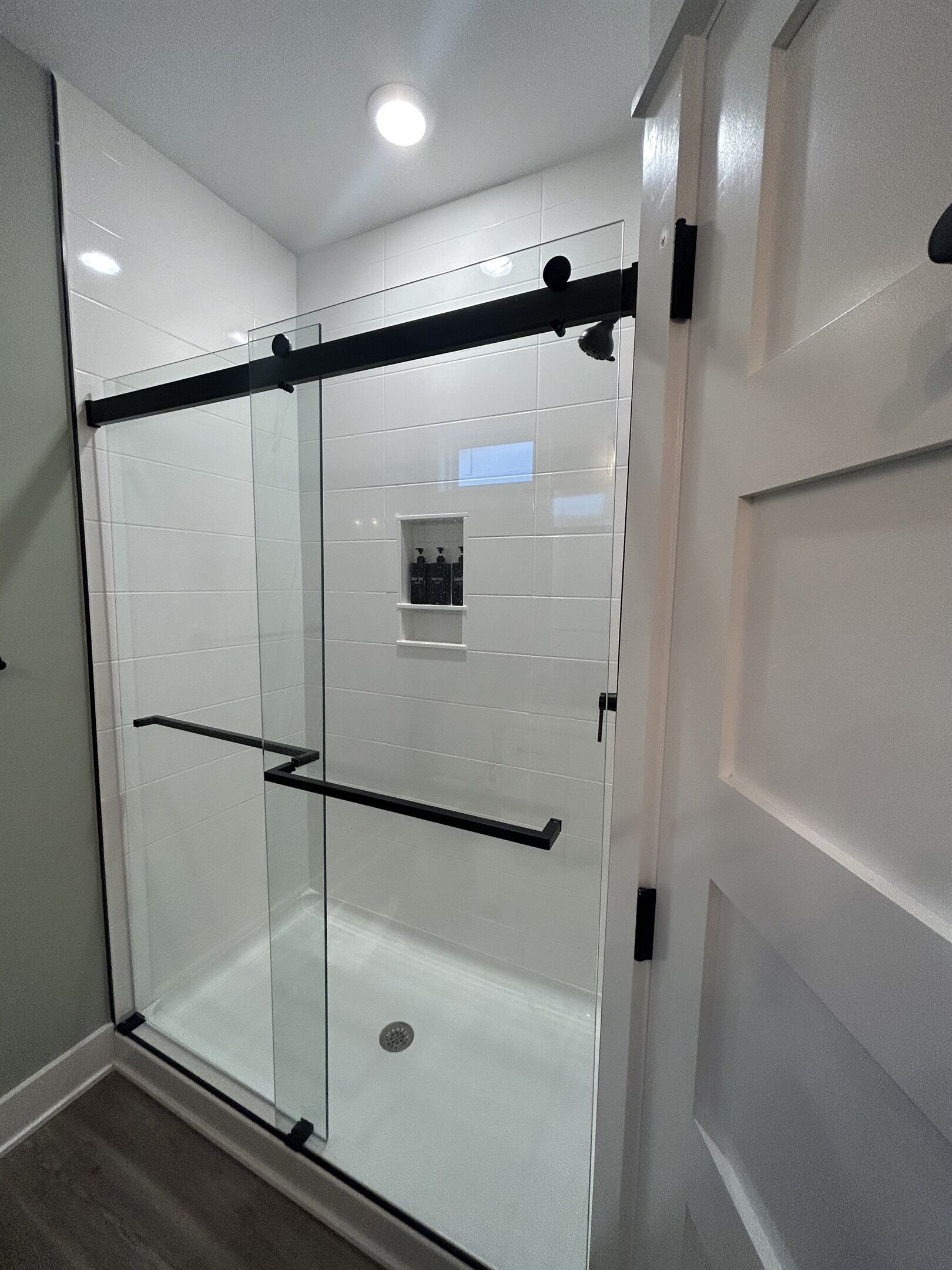 Un baño moderno con cabina de ducha de vidrio, un perchero negro y un estante pequeño con artículos de aseo.