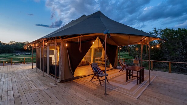 A tented accommodation with a wooden deck, a seating area with chairs and a table, and a view of the surrounding landscape.