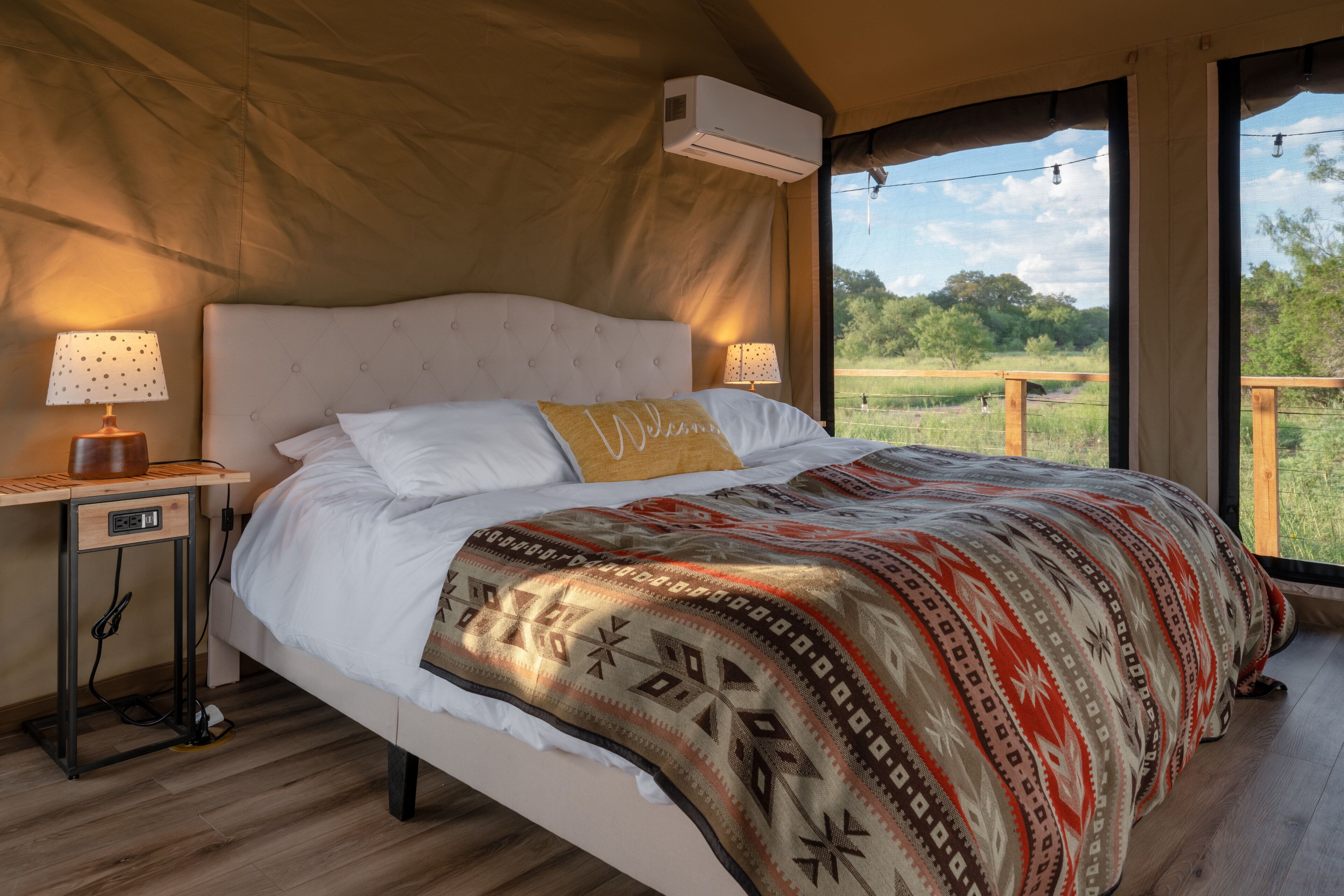 Un dormitorio con cama, dos mesitas de noche con lámparas, un equipo de aire acondicionado y vistas al exterior.