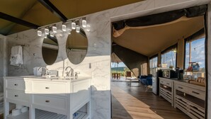 A modern bathroom with a large vanity, double sinks, and a large mirror. There is a wooden floor and a view of the outdoors through large windows.