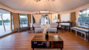 Una habitación con tienda de campaña, suelo de madera, dos sillones blancos, una mesa de centro de madera y un ventilador de techo.