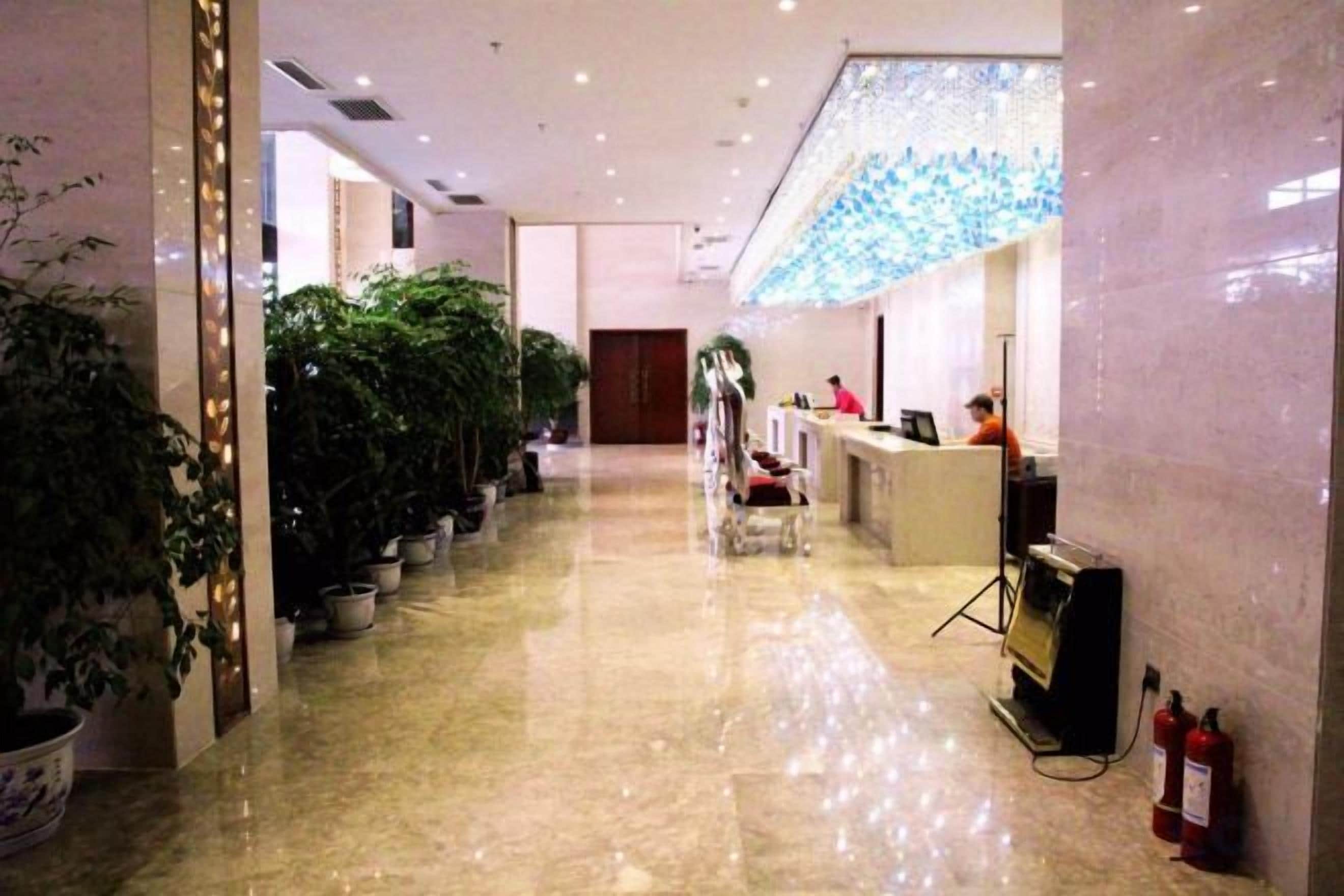 A hotel reception area with a reception desk, potted plants, and a fire extinguisher.
