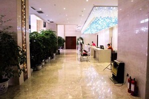 Zona de recepción de hotel con mostrador, plantas en macetas y extintor.