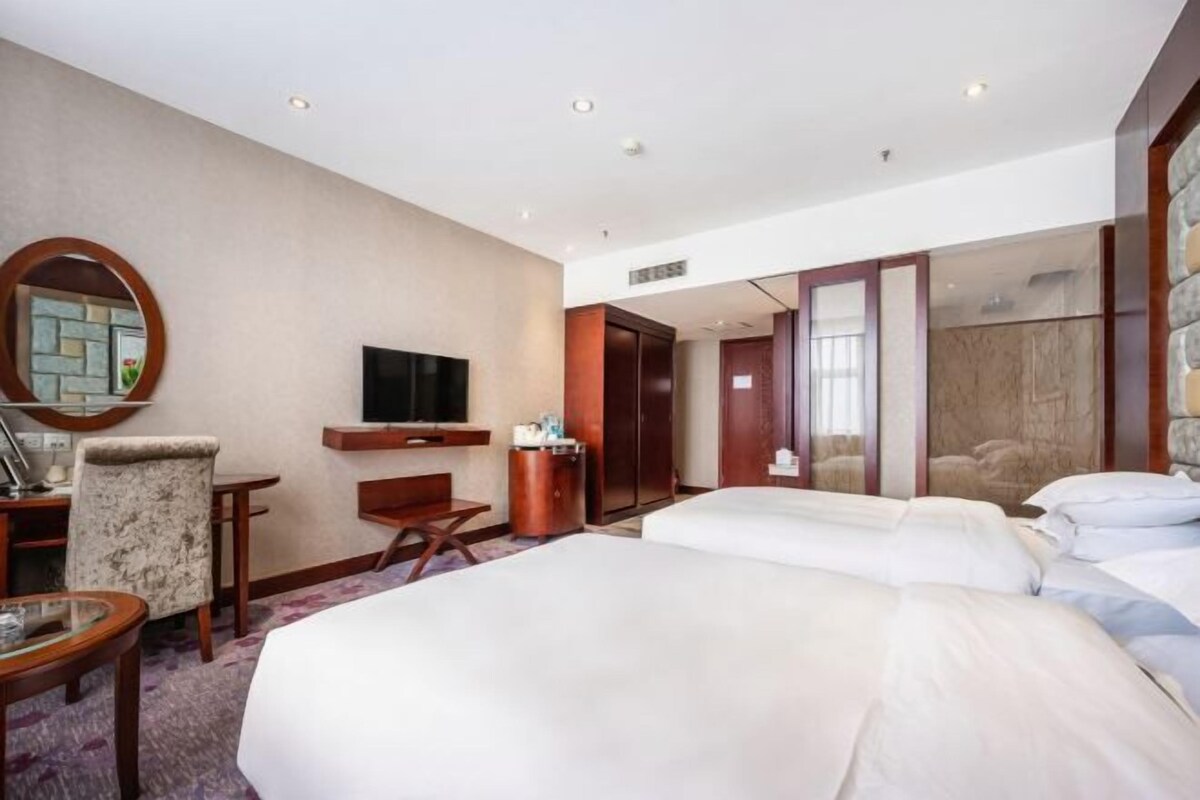 Une chambre d’hôtel avec deux lits, une télévision, un bureau, une chaise et un miroir.
