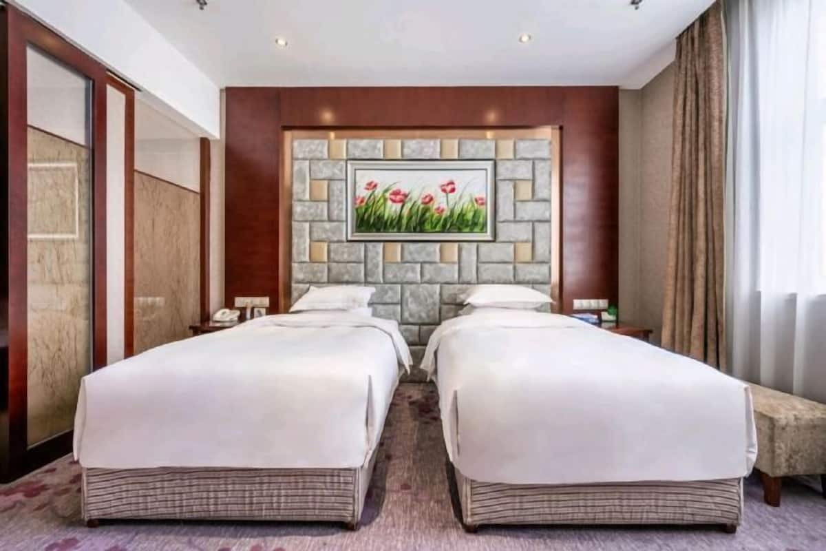 Een hotelkamer met twee bedden, een accentmuur van steen, een schilderij van bloemen en uitzicht op het omliggende landschap.