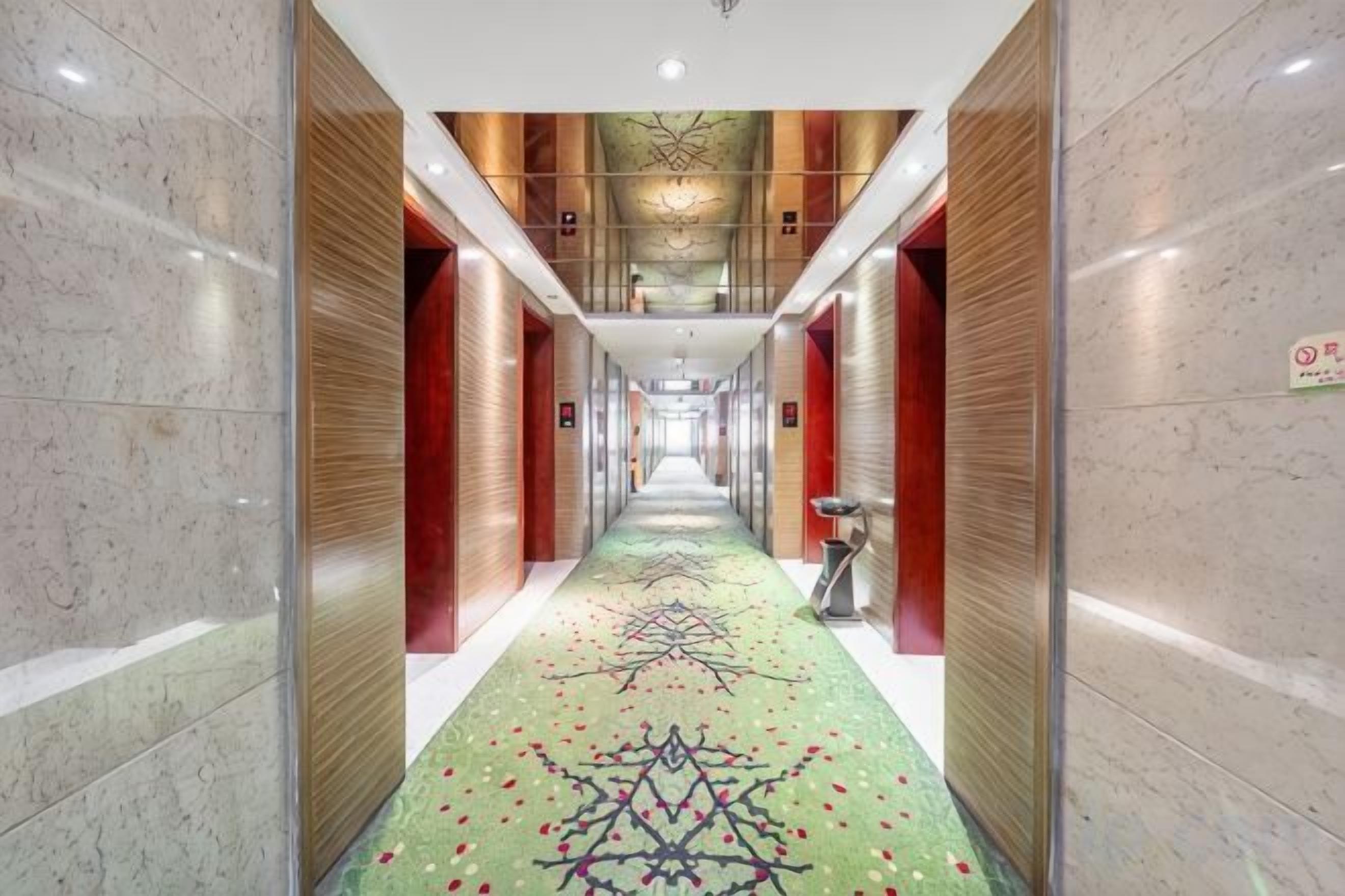 Un pasillo con alfombra estampada, paneles de madera y un espejo grande.