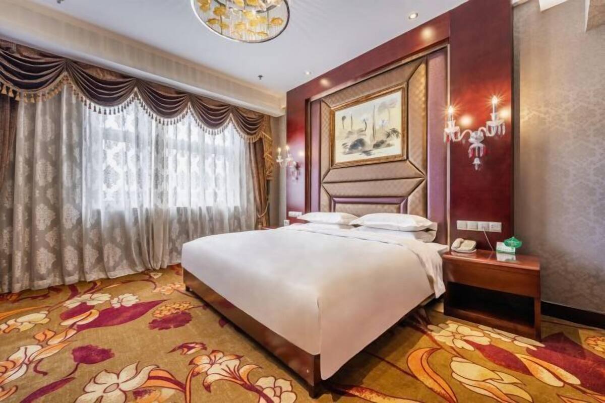 Een hotelkamer met een groot bed, een nachtkastje met telefoon, en een schilderij aan de muur.