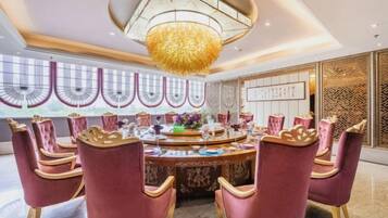 A dining area with a round table, red upholstered chairs, and a large chandelier.