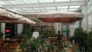 Een kas-achtig vertrek met tafels, stoelen, potplanten en grote parasols.
