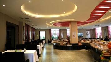 Een restaurantgedeelte in een hotel met ronde tafels, een bar in het midden en uitzicht op het omliggende landschap.