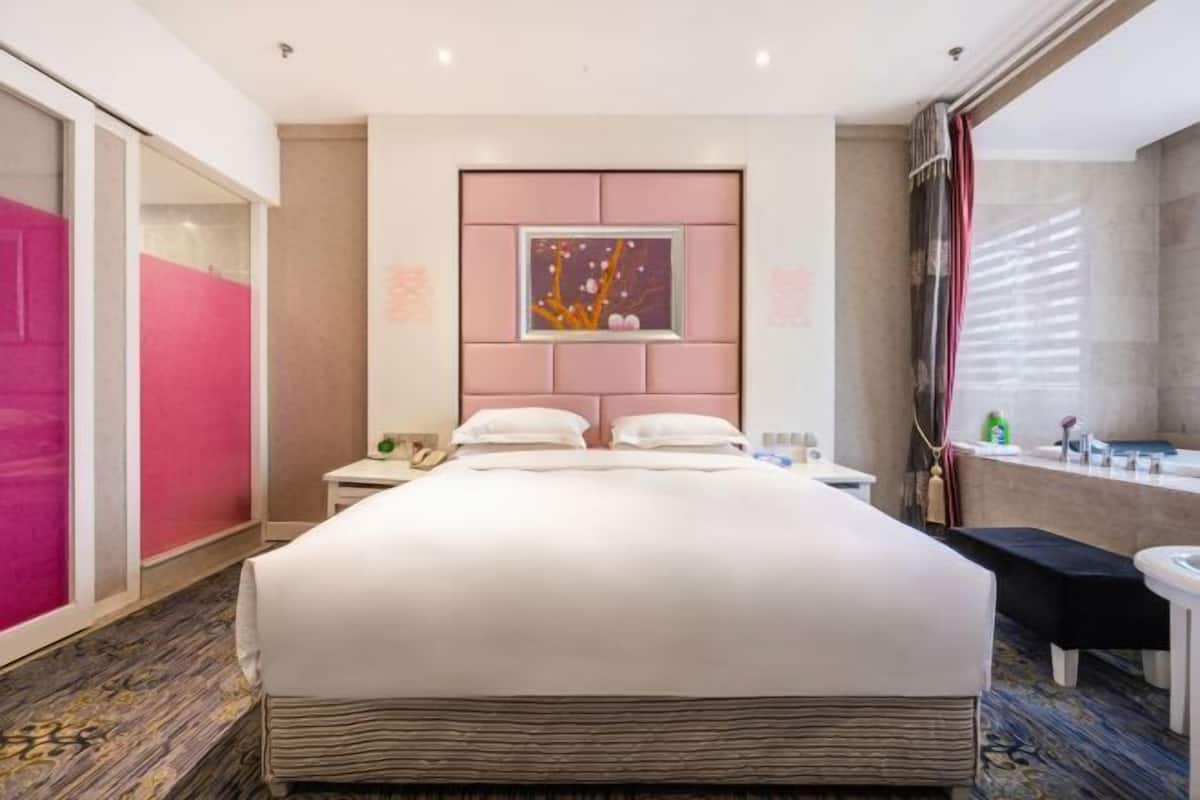 Hotelkamer met een groot bed, nachtkastje, badkamer met badkuip, en raam met jaloezieën.