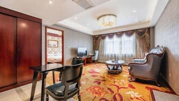 Una habitación de hotel con zona de comedor, candelabro, ventana grande con cortinas y suelo alfombrado.