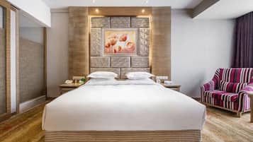 A hotel room with a large bed, a nightstand with a phone, a chair, and a wall with a framed picture.