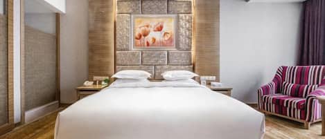 A hotel room with a large bed, a nightstand with a phone, a chair, and a wall with a framed picture.