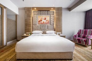 Une chambre d’hôtel avec un grand lit, une table de chevet avec un téléphone, une chaise et un mur orné d’un tableau.