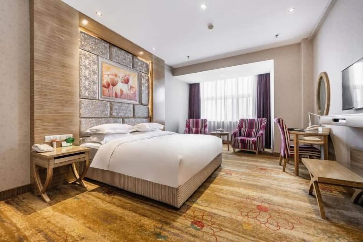 Een hotelkamer met een groot bed, een bureau, een stoel, een televisie en een raam met gordijnen.