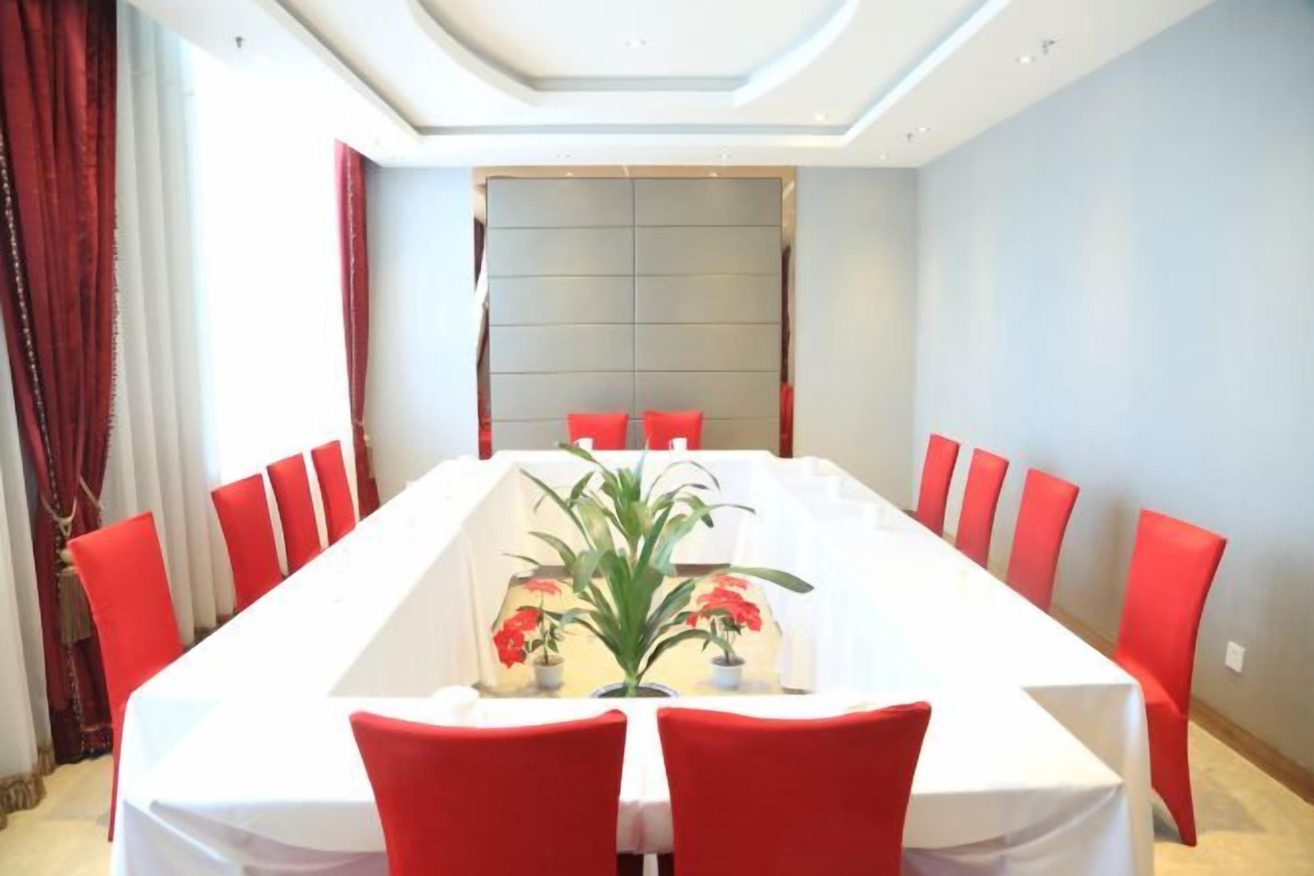 Un salón de conferencias con una larga mesa, sillas rojas y un mantel blanco.