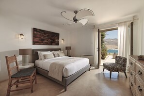 A bedroom with a bed, a chair, a dresser, a ceiling fan, and a view of the outdoors.